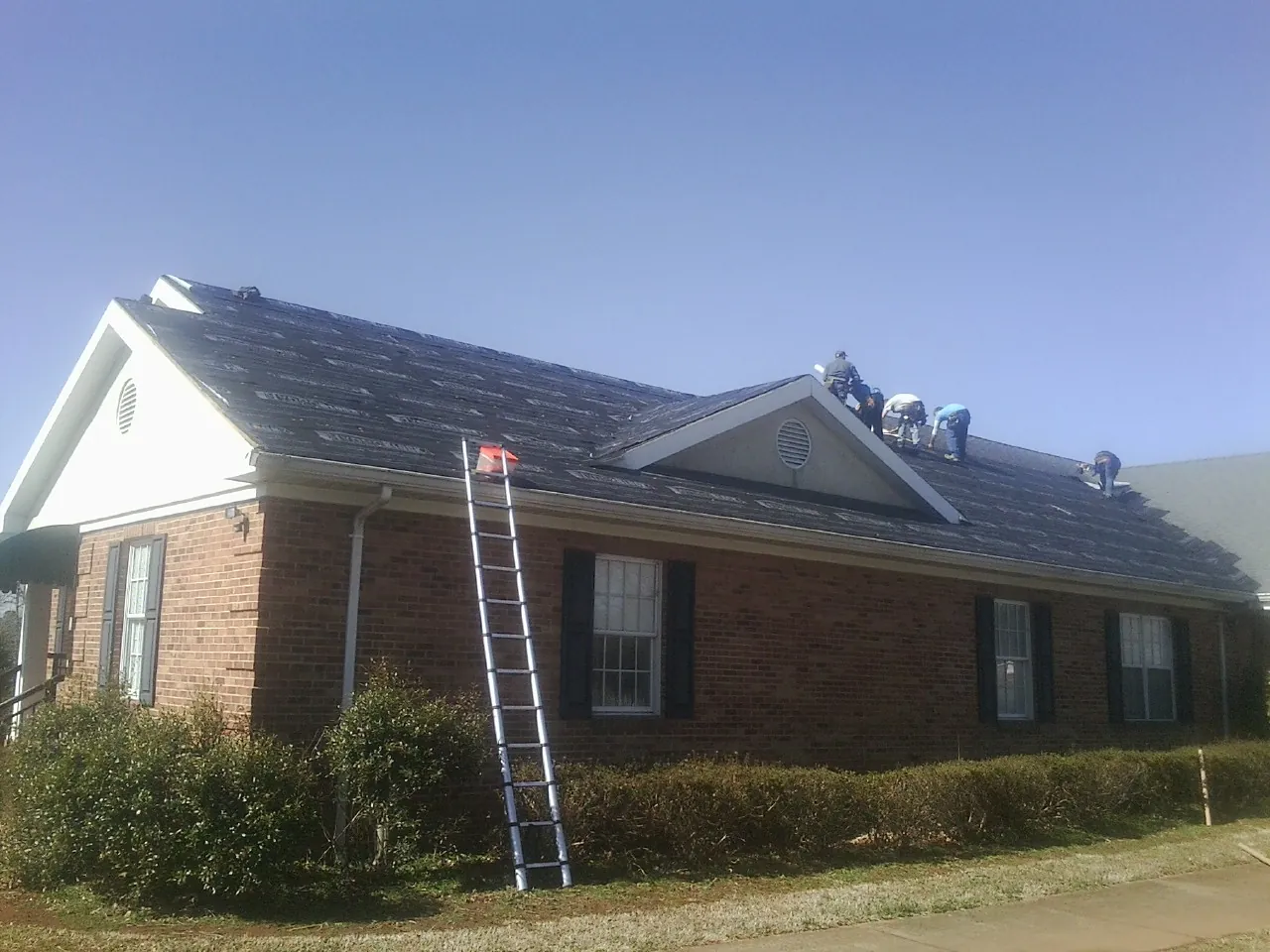 Crew tearing shingles off a brick ranch roof with a ladder set — Emergency Roof Repair work by our crew in Newhall