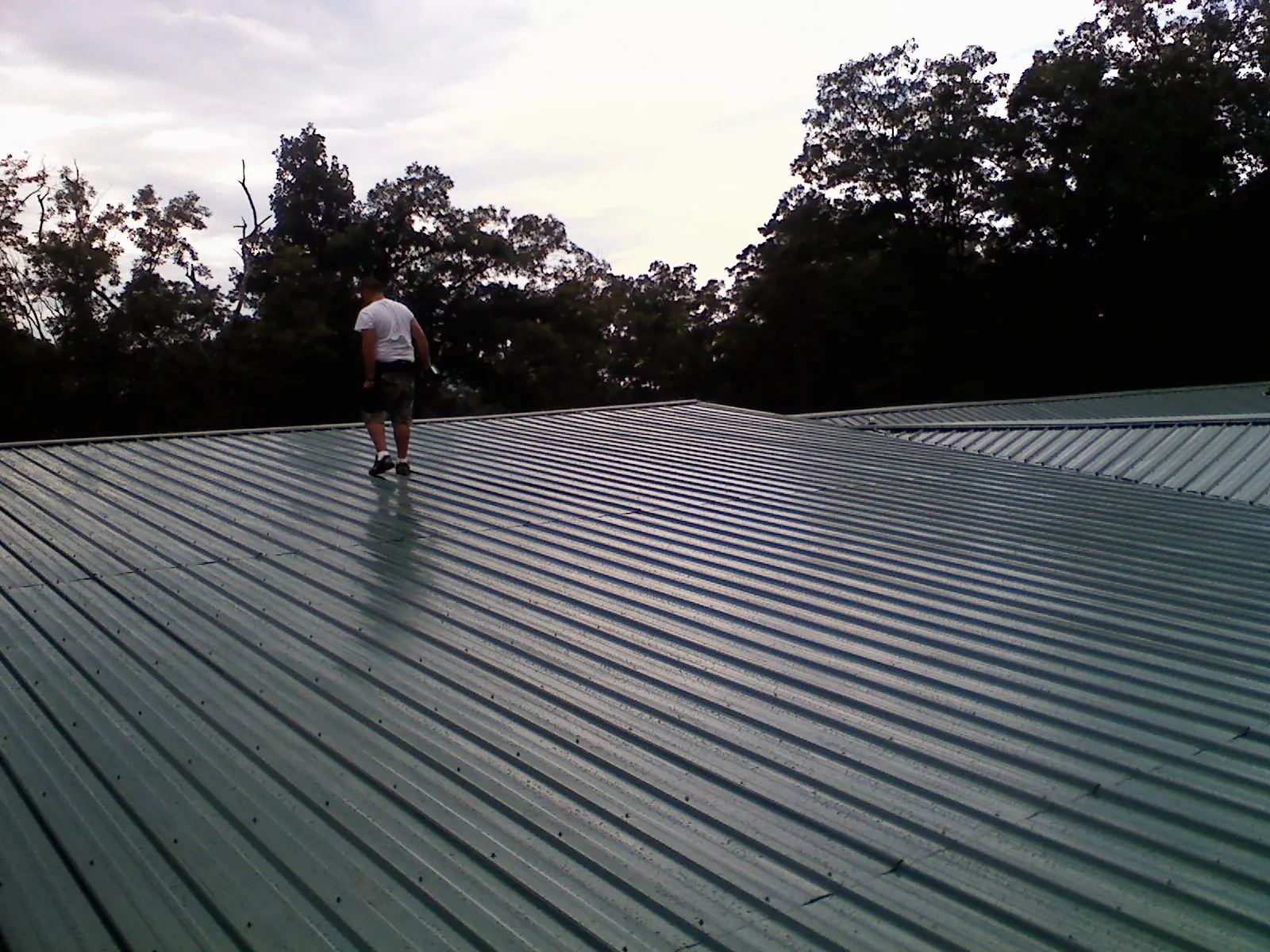 Roofer walking a wide expanse of new green metal roofing in Newhall