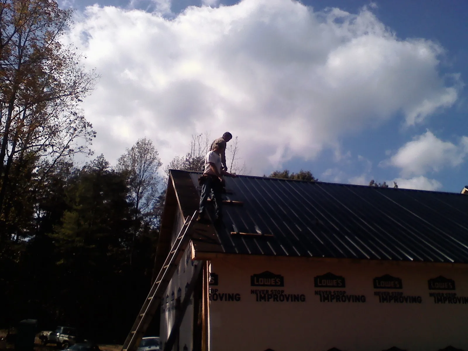 Roofer fastening dark metal panels high against a cloudy sky, from a Roof Inspection job in Newhall