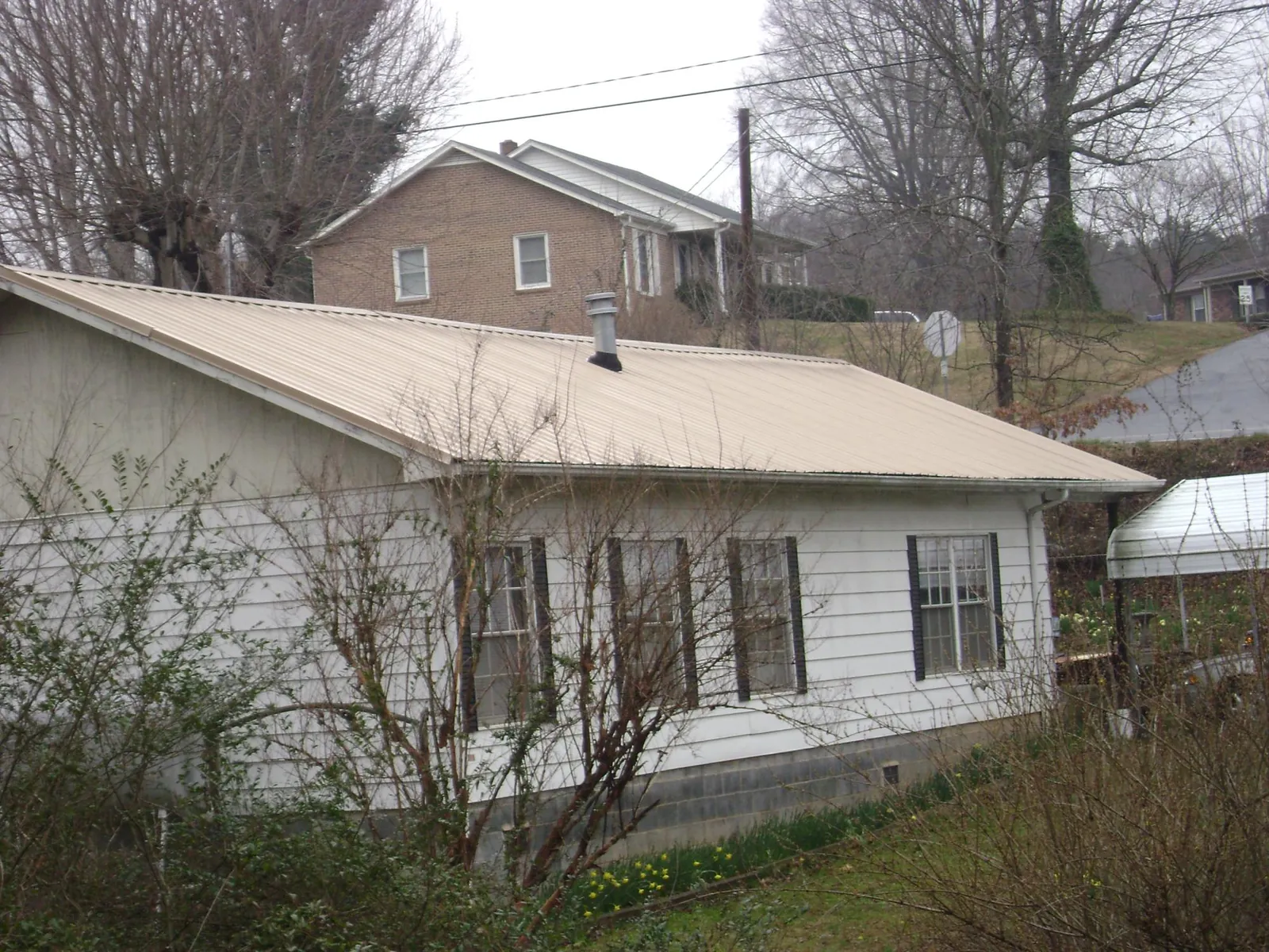 Tan metal roof on a white sided house set into a hillside — Commercial Roofing by Roofing Brothers in Newhall